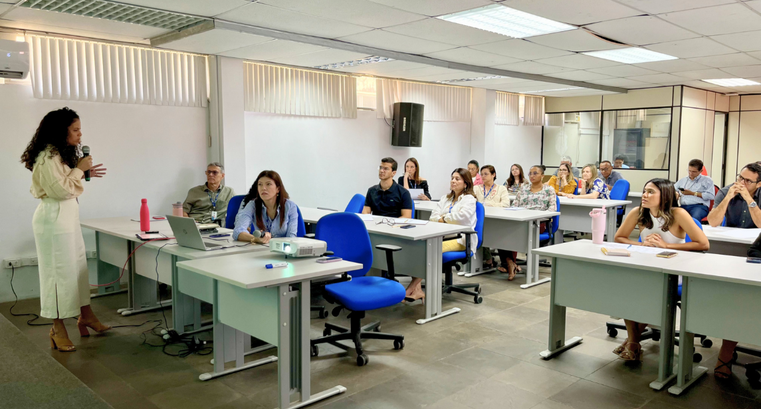 Imagem da sala com as mesas e os servidores sentados assistindo a apresentação