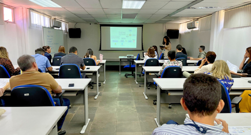 Imagem da sala com as mesas e os servidores sentados assistindo a apresentação